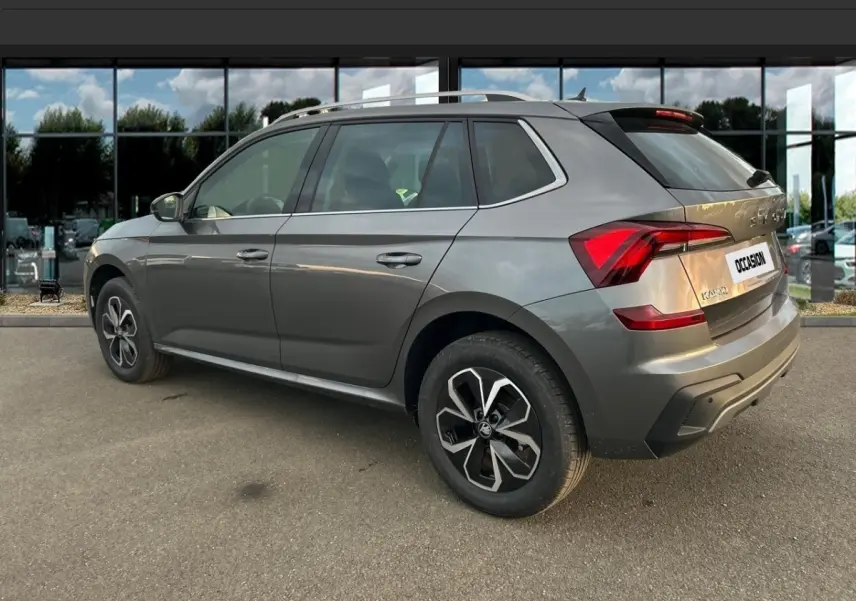 Vue 3/4 arrière droite d'un Skoda Kamiq gris clair avec jantes alliage et feux arrière LED, stationné devant une vitrine.