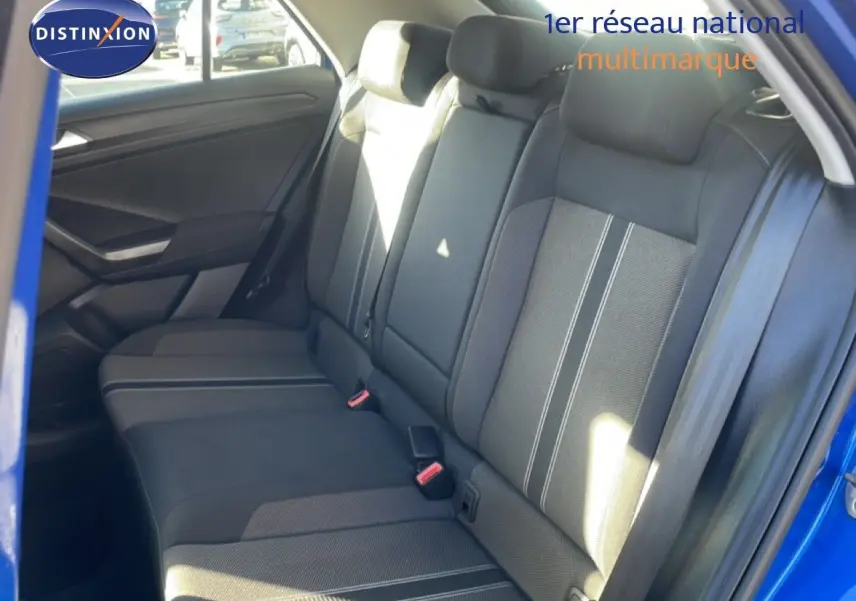 Vue intérieure côté arrière droit du Volkswagen T-Roc bleu Ravenna, montrant les sièges arrière en tissu gris avec surpiqûres blanches.