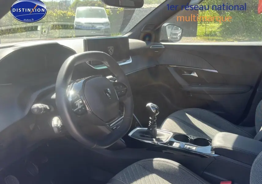 Vue intérieure côté conducteur du Peugeot 2008 1.2 100 Allure 2025 avec volant multifonction et sellerie tissu gris.