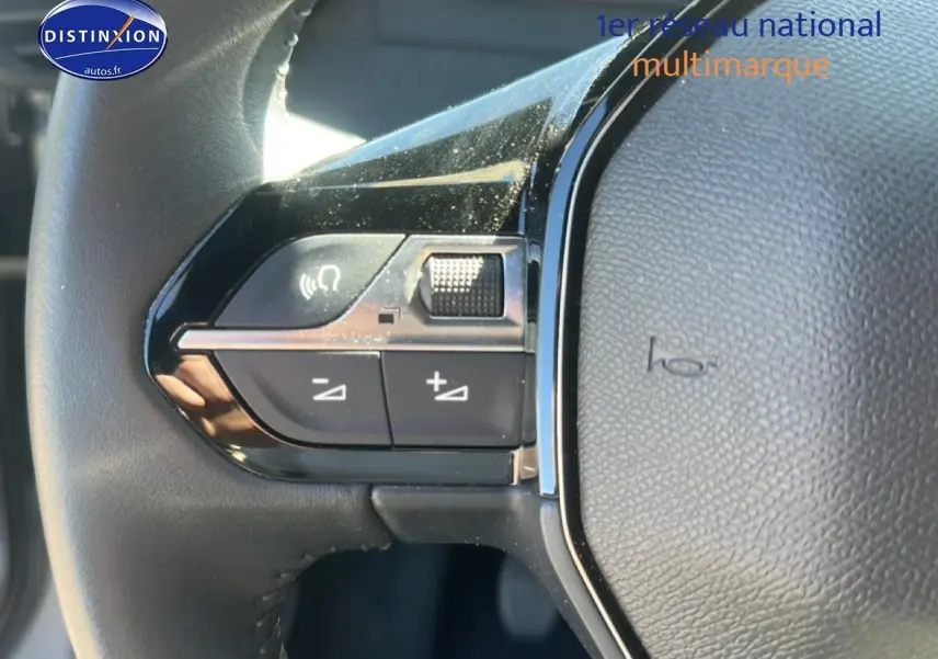 Gros plan sur les commandes gauche du volant noir du Peugeot 2008 1.2 100 Allure gris Artense, avec boutons multifonctions.
