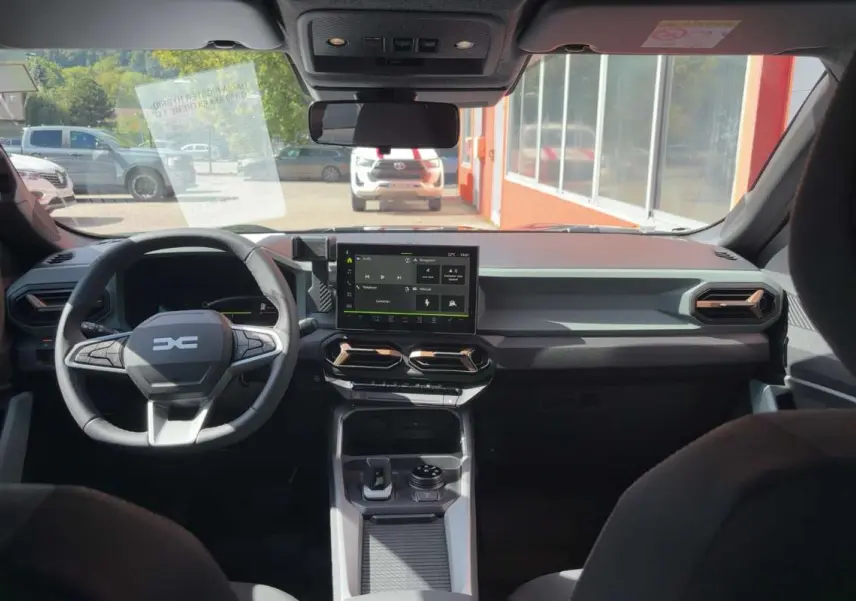 Vue intérieure avant du tableau de bord du Dacia Bigster vert cèdre avec écran tactile et volant multifonction.