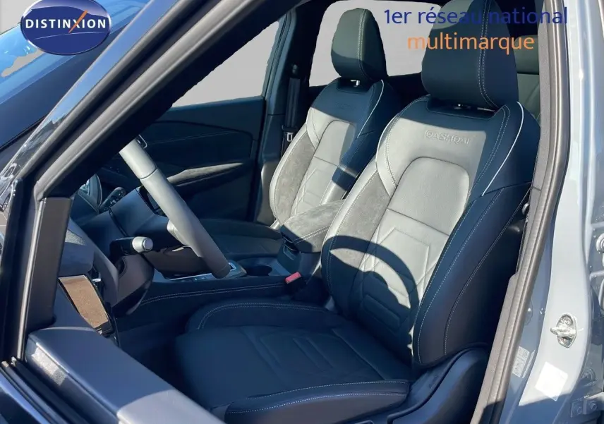 Vue intérieure côté conducteur du Nissan Qashqai gris céramique, sièges cuir noir avec logo Qashqai brodé et toit panoramique ouvert.