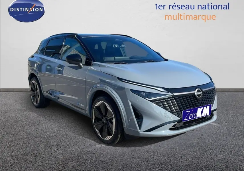 Vue de face du Nissan Qashqai gris céramique métal avec calandre noire et phares LED allumés dans un showroom.