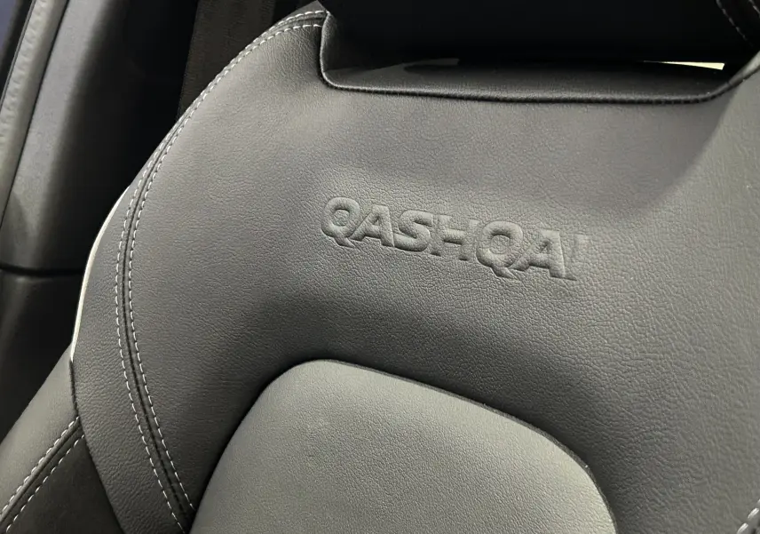 Gros plan sur l'appui-tête noir en cuir embossé du Nissan Qashqai 2025, soulignant le logo du modèle.