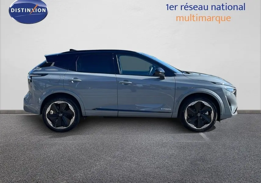 Nissan Qashqai gris céramique métal vu en 3/4 avant droit avec phares allumés et calandre noire distinctive.