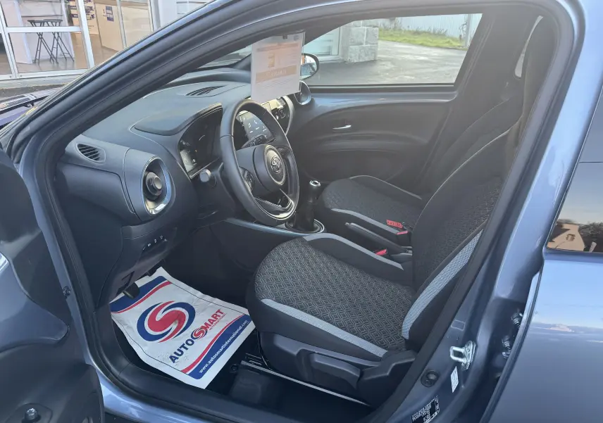 Vue intérieure côté conducteur de la Toyota Aygo X bleu 2025, avec volant, sièges tissu et boîte manuelle visible.