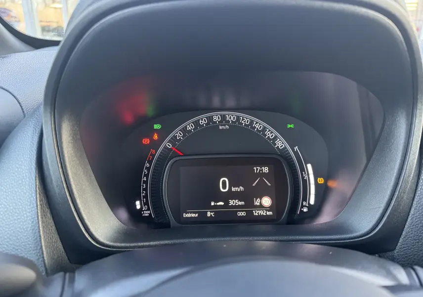 Vue rapprochée du tableau de bord numérique de la Toyota Aygo X 2025, affichant la vitesse à 0 km/h et divers voyants allumés.
