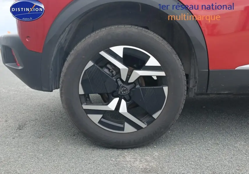 Gros plan sur la roue avant gauche et la jante alu noire et argentée du Peugeot 2008 rouge élixir.