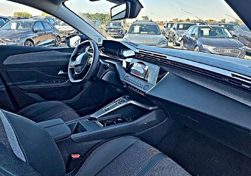 Vue intérieure côté conducteur de la Peugeot 308 SW 2025, montrant le tableau de bord moderne et la console centrale noire.