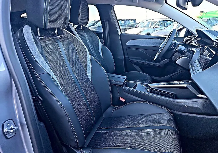 Vue intérieure côté conducteur de la Peugeot 308 SW 2025 gris artense, avec sièges tissu et cuir et accoudoir central.