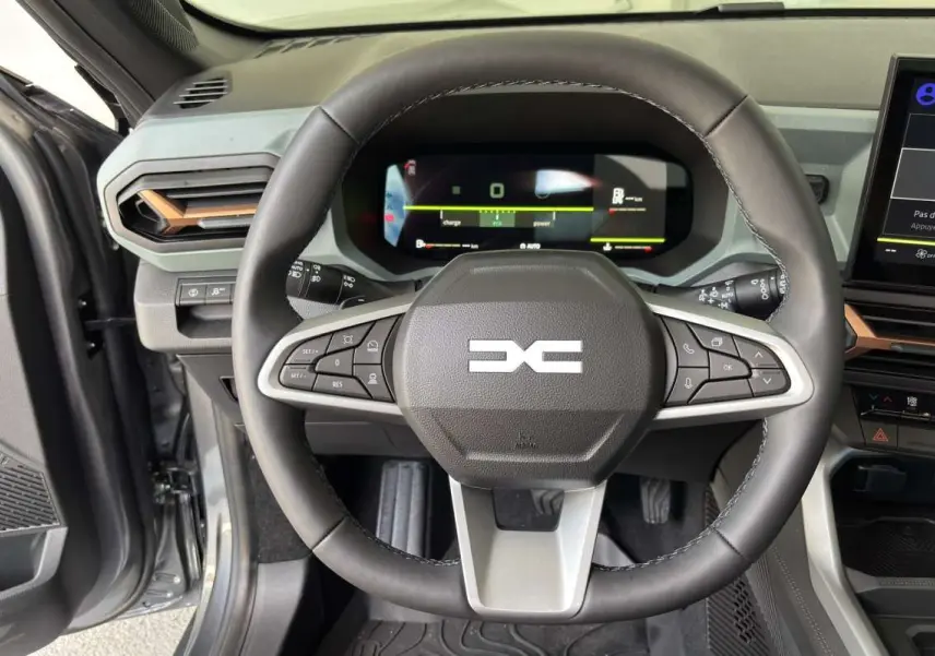 Vue intérieure centrée sur le volant cuir noir du Dacia Bigster Hybrid-G 150, avec tableau de bord digital et écran tactile.