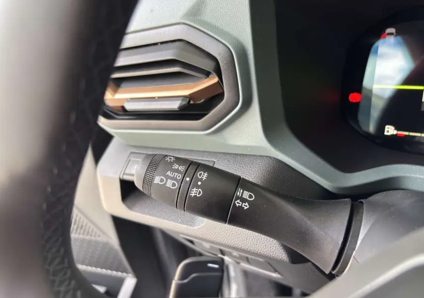 Gros plan sur la commande des phares et clignotants à gauche du volant dans le tableau de bord gris du Dacia Bigster Hybrid-G 150.