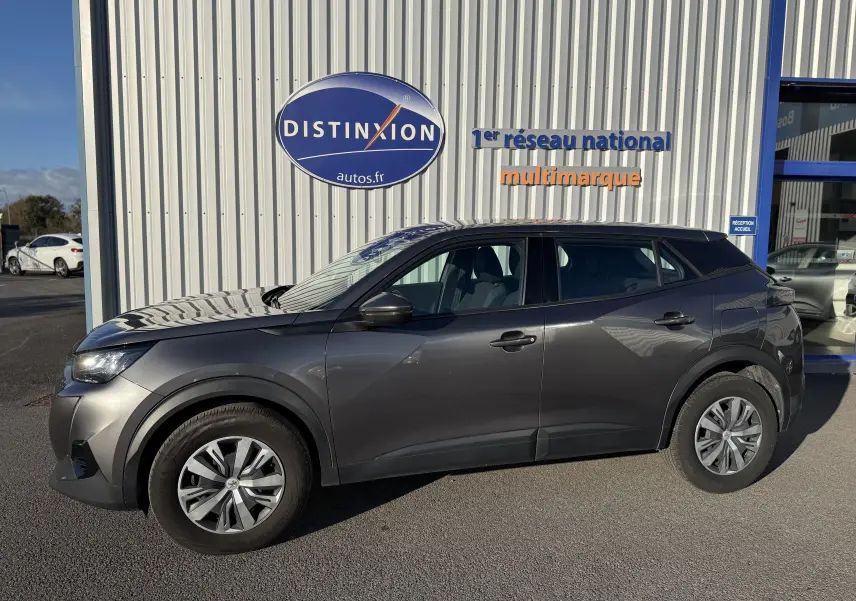 Peugeot 2008 gris vue de profil côté gauche, SUV compact stationné devant un mur avec logo Distinxion.