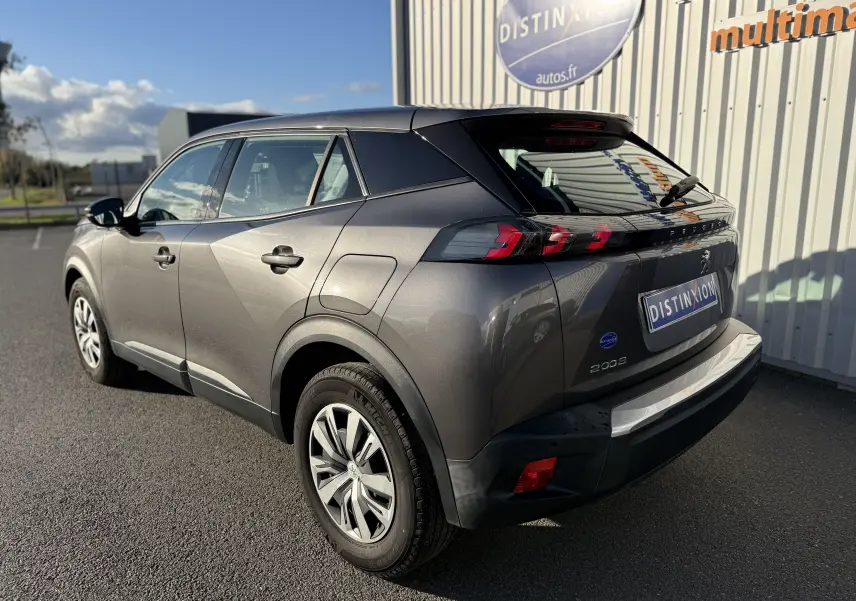 Peugeot 2008 gris vue 3/4 arrière droit, avec feux arrière LED et jantes alliage, stationné devant un bâtiment.