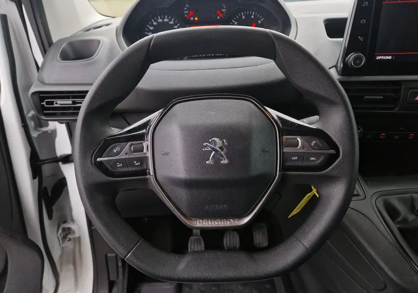 Vue rapprochée du volant noir du Peugeot Partner blanc 2020, avec commandes intégrées et tableau de bord visible en arrière-plan.