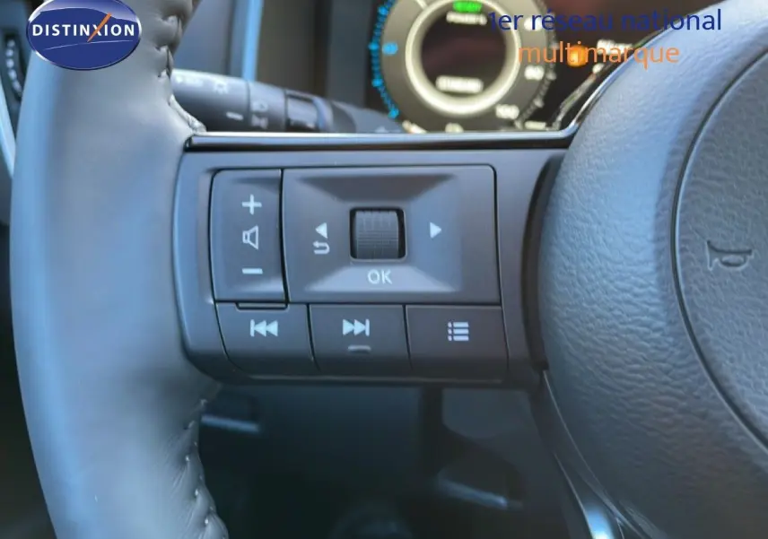 Gros plan sur les commandes gauche du volant cuir noir du Nissan Qashqai 2025, tableau de bord numérique en arrière-plan.