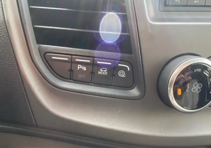 Gros plan sur les commandes de bord noires du Ford Transit Fourgon blanc, avec boutons d’aide au stationnement et mode conduite.