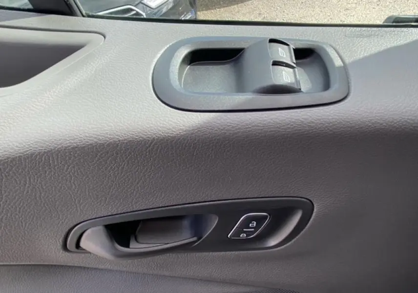 Gros plan sur la poignée intérieure et les commandes des vitres d'une porte avant droite du Ford Transit Fourgon blanc.