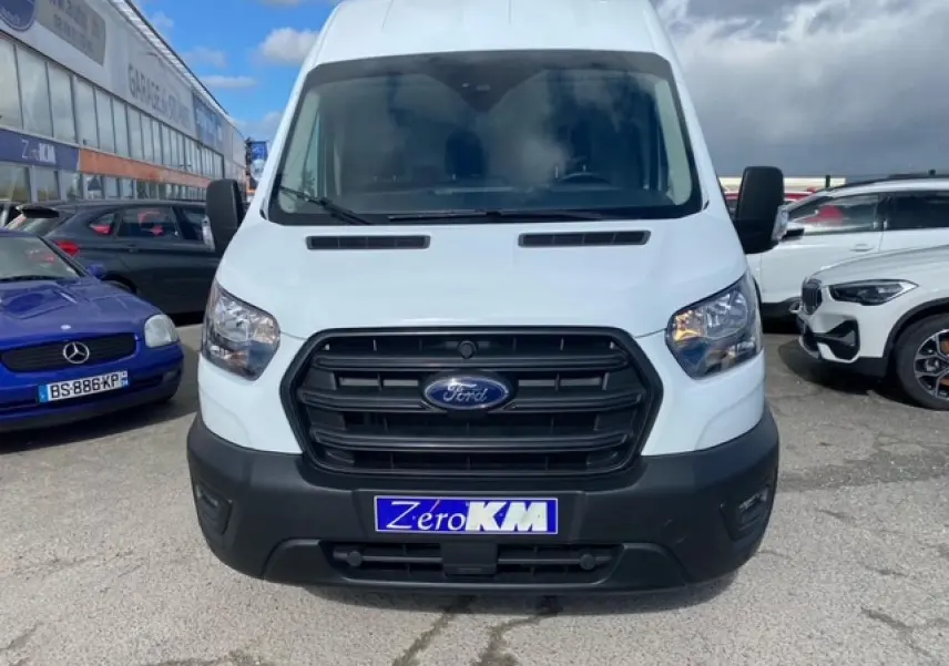 Vue avant d'un Ford Transit Fourgon blanc avec calandre noire et plaque d'immatriculation "Zéro KM" sur un parking.