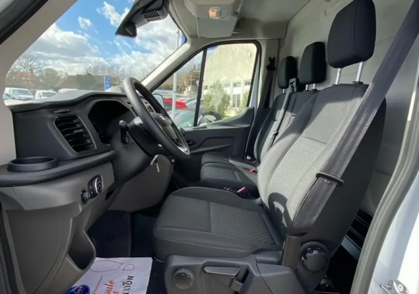 Vue intérieure côté conducteur du Ford Transit Fourgon blanc 2023, montrant les sièges avant et le tableau de bord.