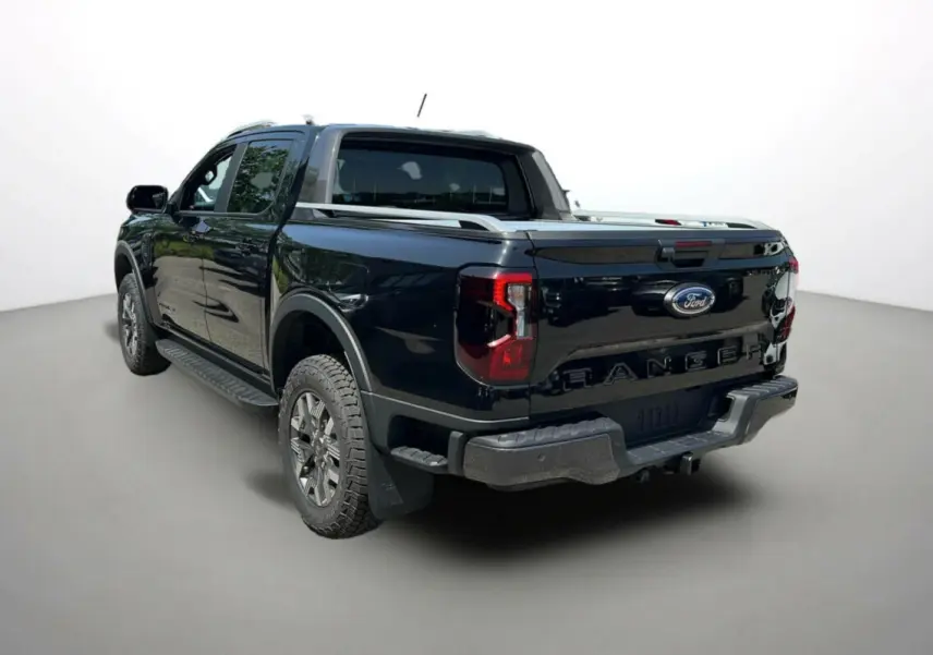 Ford Ranger PHEV noir agate vu en 3/4 arrière droit, avec barres de toit et jantes alu tout-terrain.
