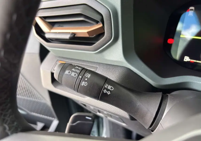 Gros plan sur la commande des feux à gauche du volant du Dacia Bigster Hybrid-G 150 vert cèdre, intérieur moderne.