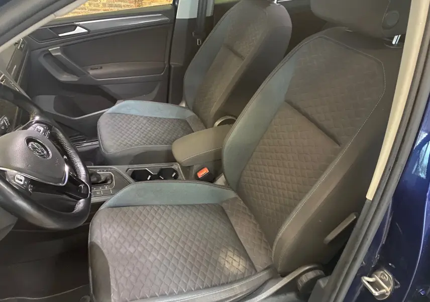 Vue intérieure côté conducteur du Volkswagen Tiguan 2020 bleu vert, sièges noirs avec surpiqûres et volant cuir.