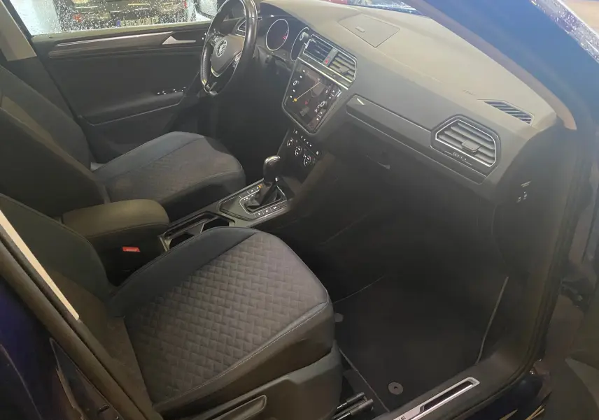 Vue intérieure côté conducteur du Volkswagen Tiguan bleu vert 2020, avec sièges noirs et console centrale équipée.