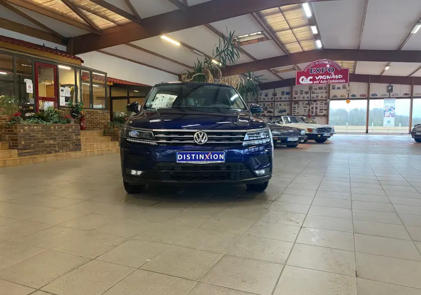 Volkswagen Tiguan iq drive bleu vert vu de face dans un showroom avec plusieurs voitures anciennes en arrière-plan