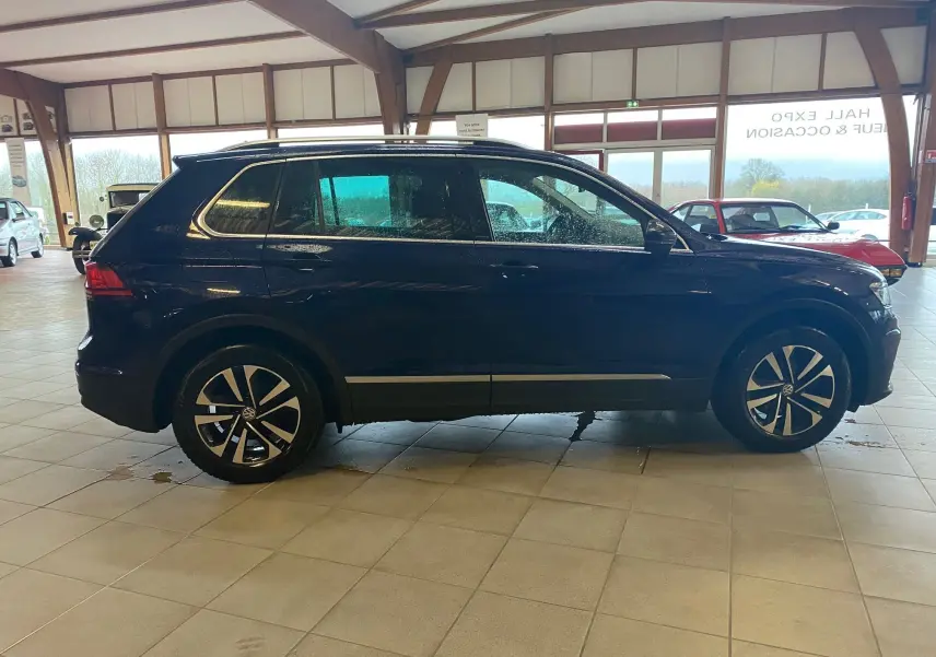 Volkswagen Tiguan iq drive bleu vert vu de profil côté gauche dans un showroom lumineux avec jantes noires.
