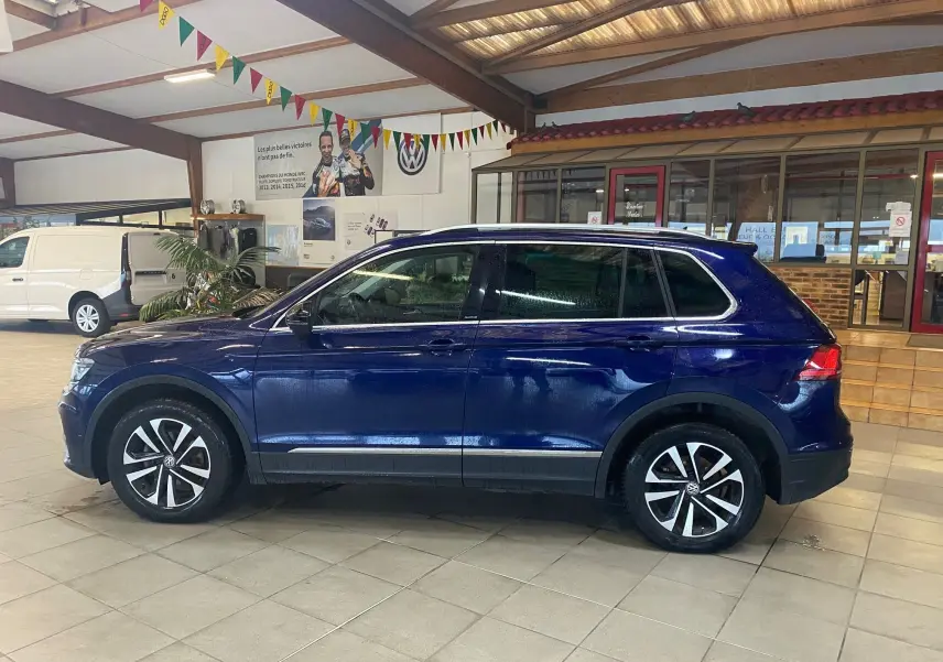 Volkswagen Tiguan iq drive bleu vert vu de profil côté gauche dans un showroom intérieur lumineux.