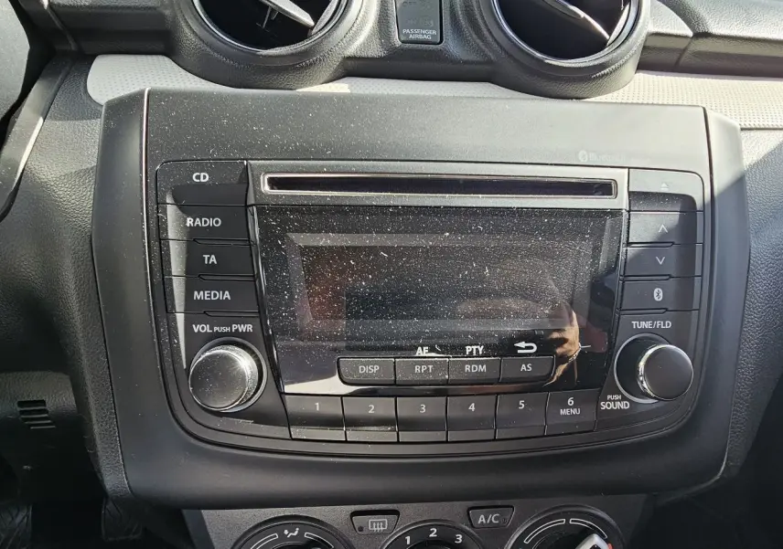 Gros plan sur la console centrale noire de la Suzuki Swift 2023, avec radio et commandes climatisation visibles.