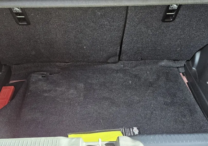 Coffre spacieux de la Suzuki Swift 1.2 Dualjet Hybrid 2023 en rouge Fervent, avec tapis noir et rangement intégré.