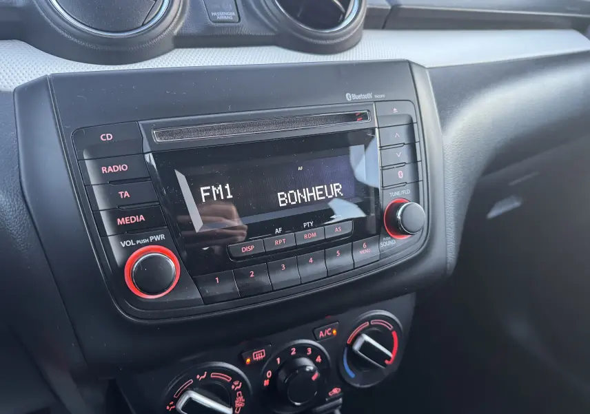 Vue rapprochée du tableau de bord noir de la Suzuki Swift 1.2 Dualjet Hybrid 2021 avec radio affichant "FM1 BONHEUR".