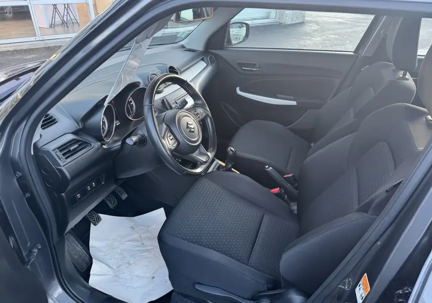 Vue intérieure côté conducteur de la Suzuki Swift gris 2021, montrant le volant, la boîte manuelle et les sièges noirs.