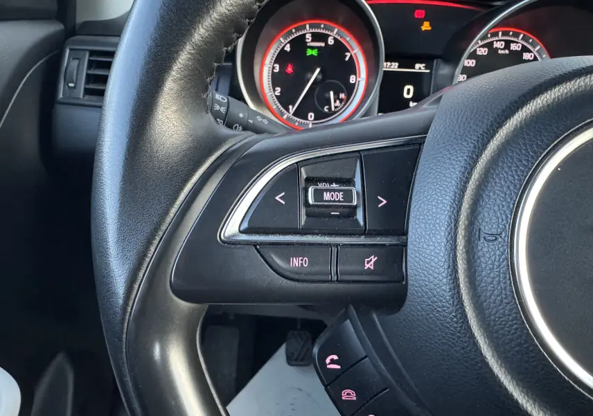 Gros plan sur le volant côté gauche de la Suzuki Swift 1.2 Dualjet Hybrid 2021 avec commandes audio et tableau de bord éclairé.