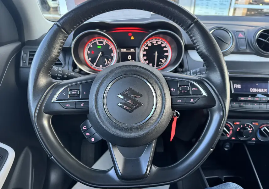 Vue intérieure centrée sur le volant noir de la Suzuki Swift 1.2 Dualjet Hybrid 2021 avec tableau de bord et commandes visibles.