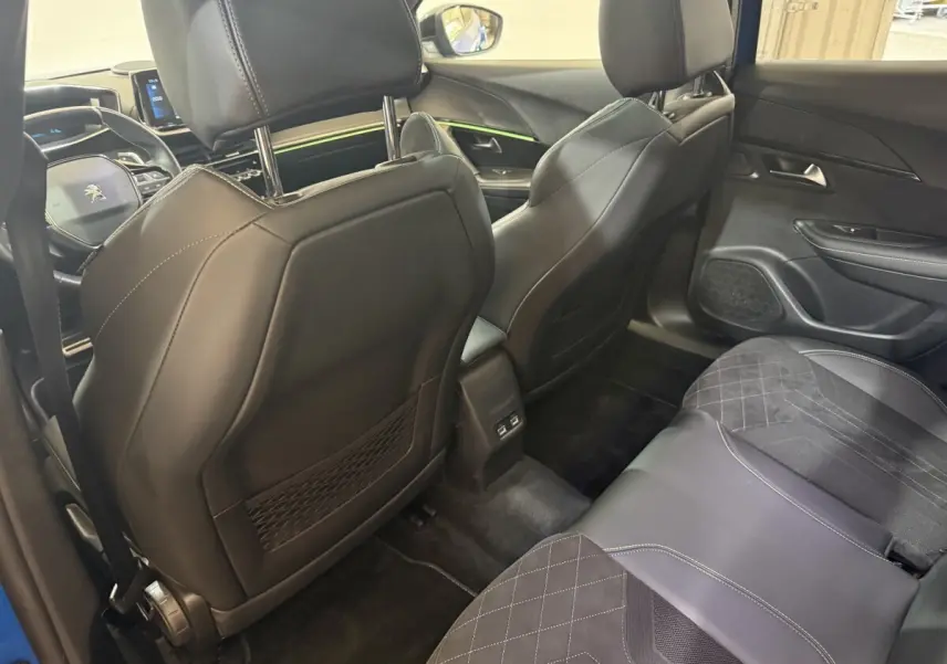 Vue intérieure arrière droite du Peugeot 2008 Bleu, sièges en cuir noir avec surpiqûres blanches et éclairage d'ambiance vert.