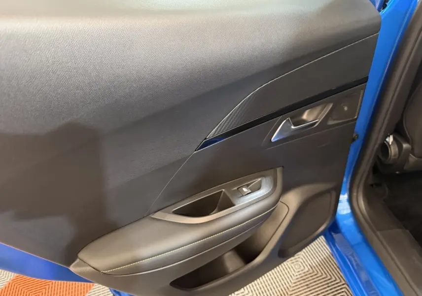 Vue rapprochée de la porte avant gauche intérieure du Peugeot 2008 bleu, avec garniture noire et bouton de fenêtre électrique.