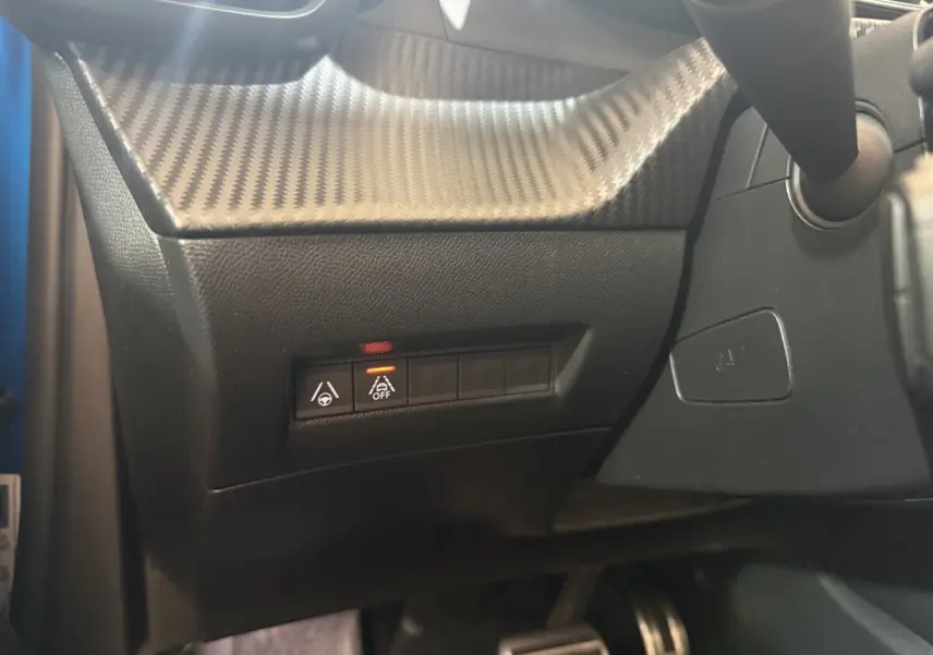 Détail du tableau de bord côté gauche avec boutons d’aide à la conduite et finition effet carbone sur Peugeot 2008 bleu.