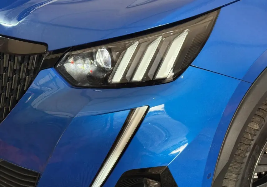 Gros plan sur le phare avant droit et la calandre d’un Peugeot 2008 bleu métallisé, détails LED visibles.