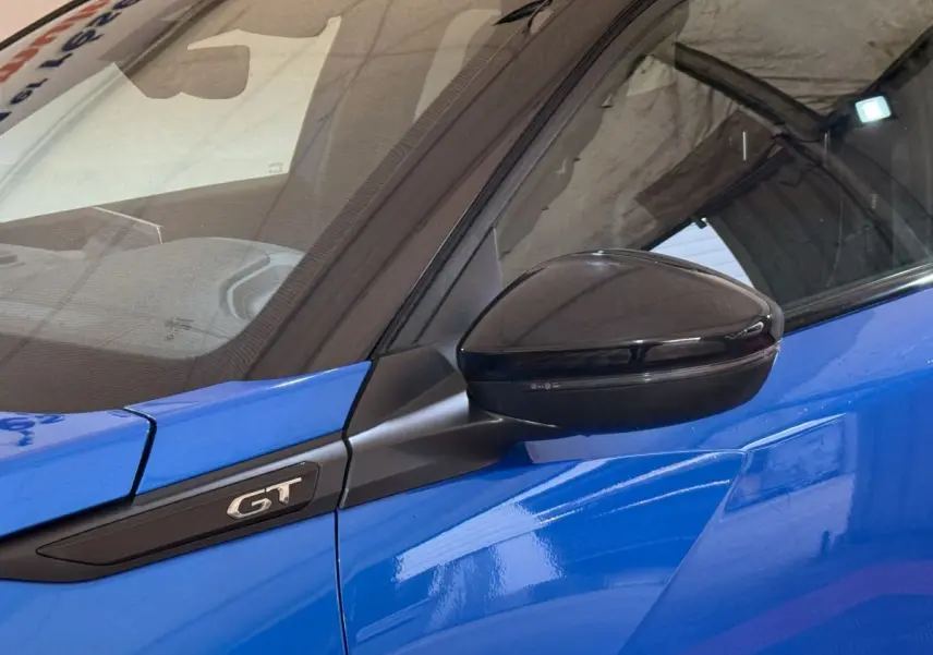 Gros plan sur le rétroviseur noir et l'emblème GT côté gauche d'une Peugeot 2008 bleu vif.