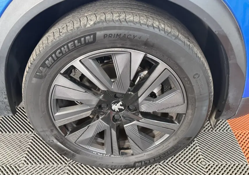 Gros plan sur la roue avant droite bleu d’un Peugeot 2008 avec jante alliage noire et grise distinctive.