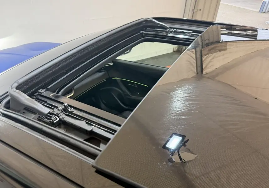 Toit ouvrant panoramique ouvert sur Peugeot 2008 bleu, vue rapprochée du mécanisme et intérieur avec éclairage d'ambiance visible.