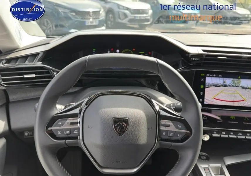 Vue intérieure centrée sur le volant cuir noir de la Peugeot 408 Hybrid 136 avec écran tactile affichant la caméra de recul.