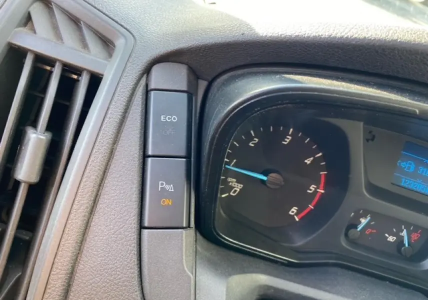 Gros plan sur le tableau de bord du Ford Transit Fourgon orange, montrant le compte-tours et les boutons de contrôle ECO et radar de stationnement.