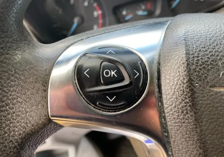 Gros plan sur les commandes noires de validation au centre du volant en cuir noir du Ford Transit Fourgon.