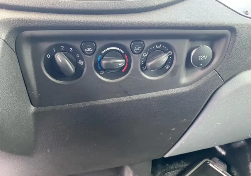 Gros plan sur les commandes de climatisation et prise 12V du tableau de bord du Ford Transit Fourgon L3H2 2015.