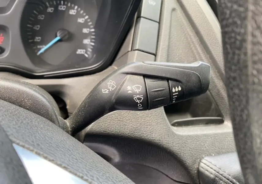 Gros plan sur la commande des essuie-glaces à droite du volant dans le tableau de bord noir du Ford Transit Fourgon orange.