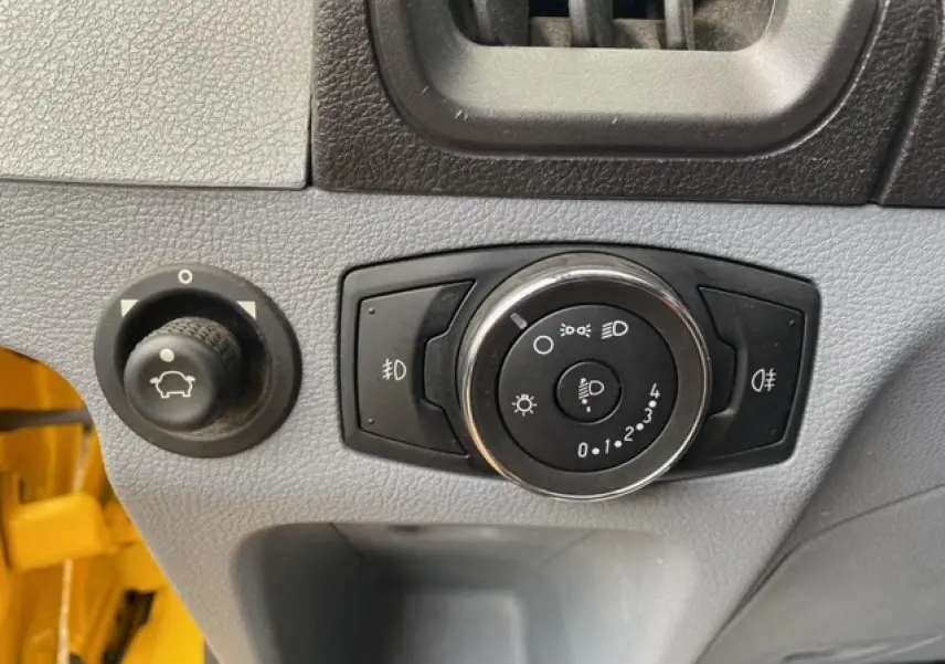 Gros plan sur les commandes d’éclairage et réglage du tableau de bord d’un Ford Transit Fourgon orange 2015.